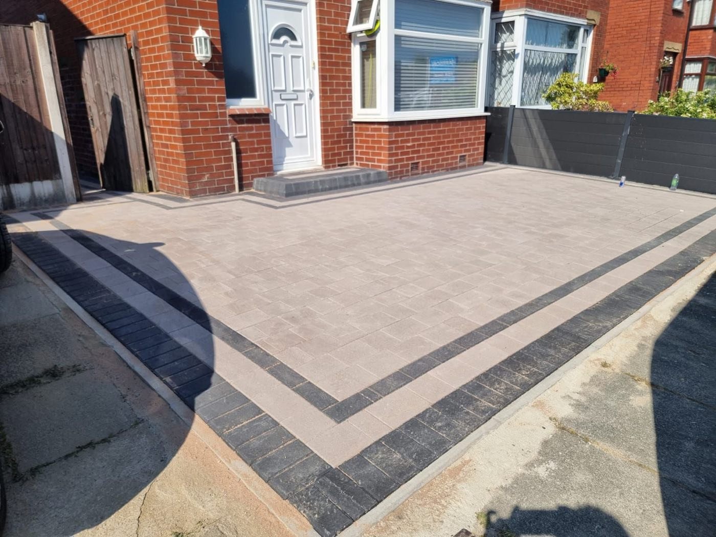 Finished buff block-paving driveway with a charcoal double border by North West Landscapes at the front of a red-brick house