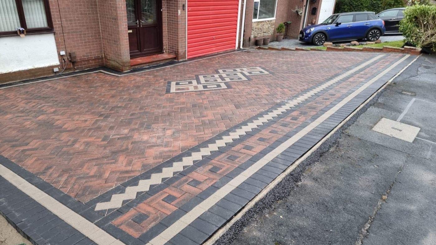 Decorative rustic block paving driveway with a Greek-key border and central diamond motif by North West Landscapes