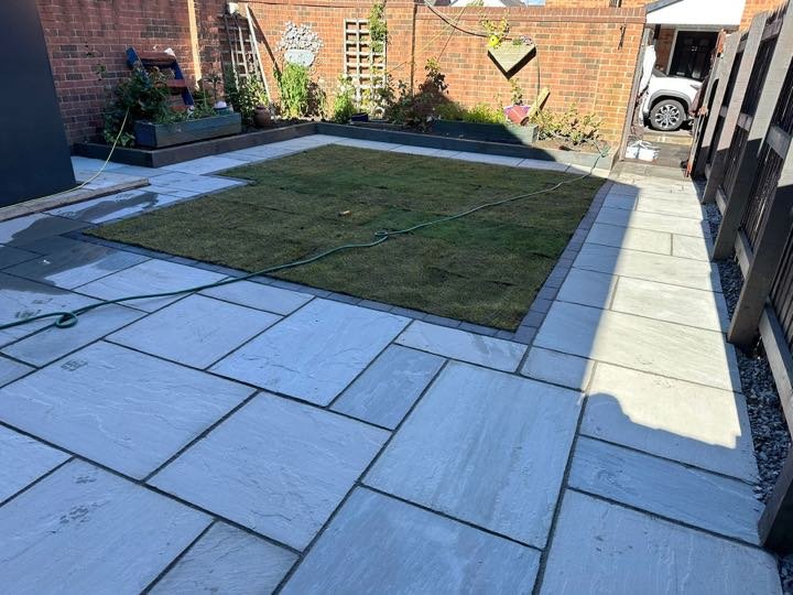 Grey Indian sandstone patio with a freshly laid turf lawn in a back garden by North West Landscapes on a sunny day