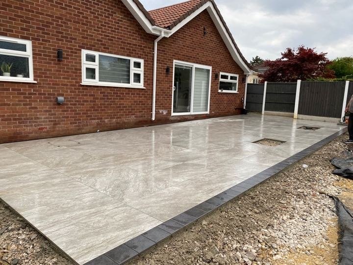 Grey marble-effect porcelain patio with a charcoal block border by North West Landscapes to the rear of a red-brick bungalow