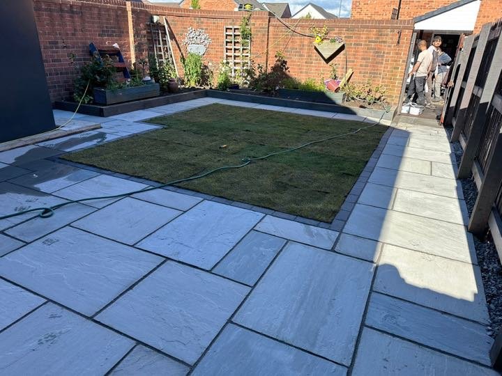 Grey Indian sandstone patio with charcoal border surrounding a new turf lawn in a back garden by North West Landscapes