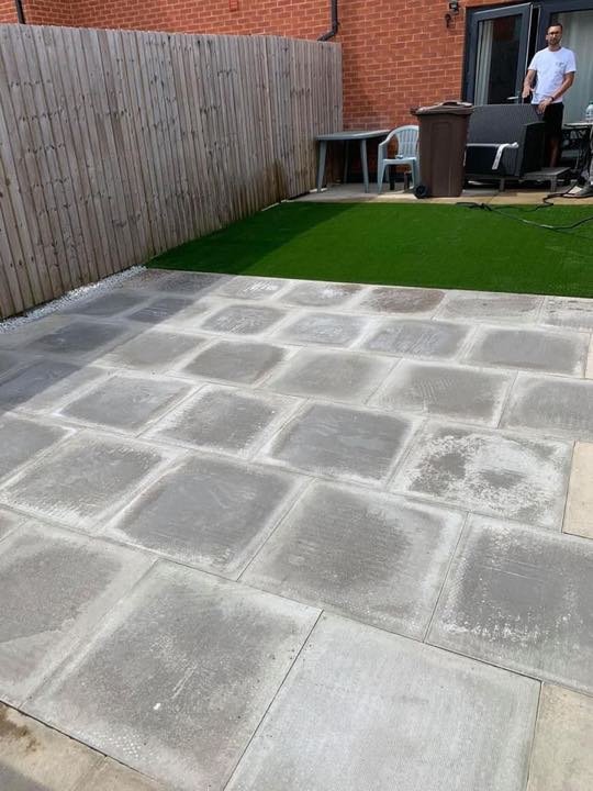 Grey concrete slab patio with artificial grass border by North West Landscapes in a small back garden