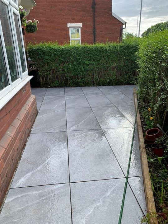 Anthracite grey porcelain patio by North West Landscapes running along the side of a house beside a hedge