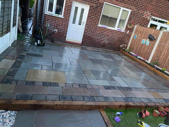 Indian sandstone riven patio with charcoal setts border and timber sleeper edging in a back garden, laid by North West Landscapes
