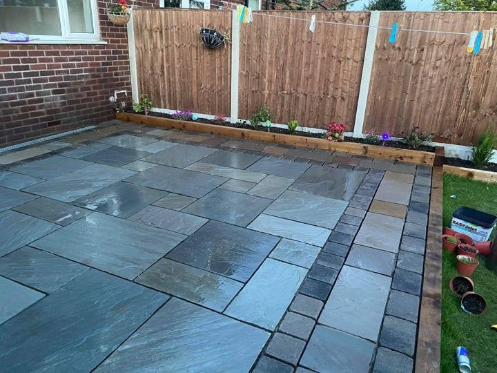 Grey Indian sandstone patio with charcoal block border and timber sleeper raised beds by North West Landscapes