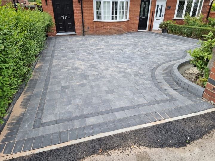 Charcoal grey block paving driveway with curved border and circular planter by North West Landscapes