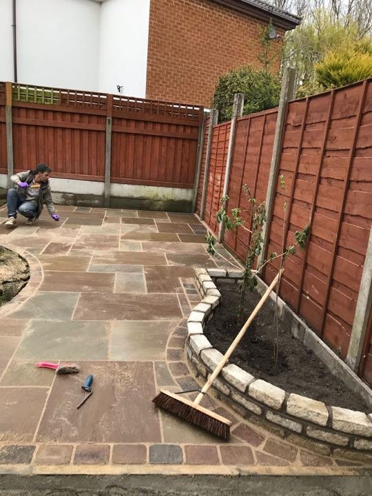 Autumn-brown Indian sandstone patio with natural stone sett raised bed edging being finished by North West Landscapes