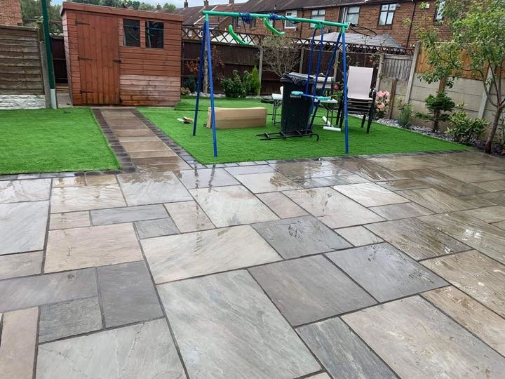 Grey Indian sandstone patio with artificial turf lawn in a back garden by North West Landscapes