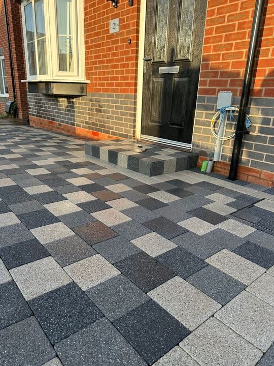 Random-mix granite block paving driveway with a charcoal step to a black front door by North West Landscapes