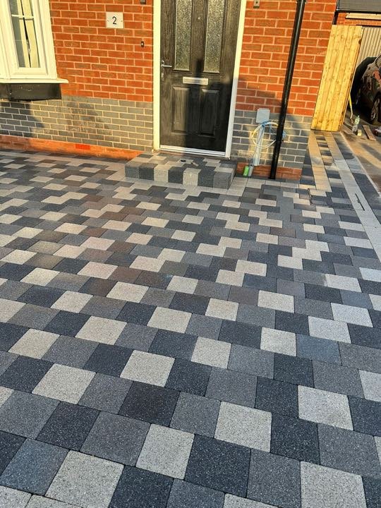 Random-mix granite block paving driveway with a charcoal step to a black door by North West Landscapes