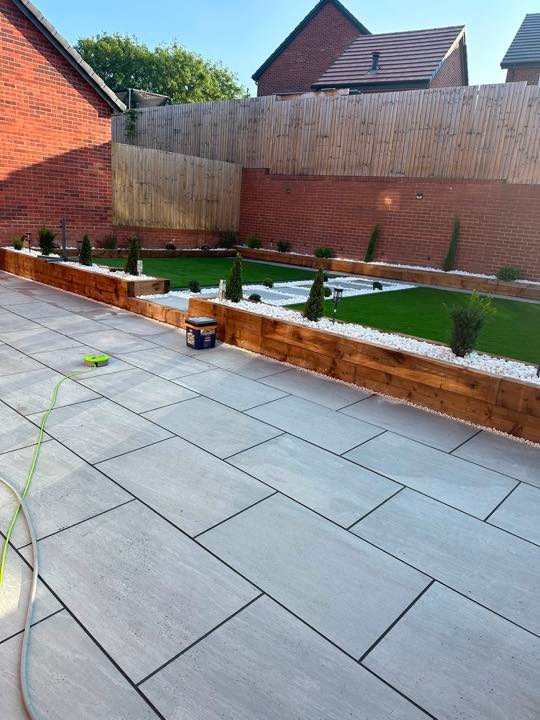 Light grey porcelain patio with timber sleeper planters and artificial lawn by North West Landscapes