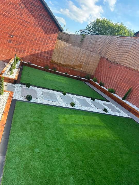 Tiered artificial lawns with porcelain stepping stones and white cobbles by North West Landscapes