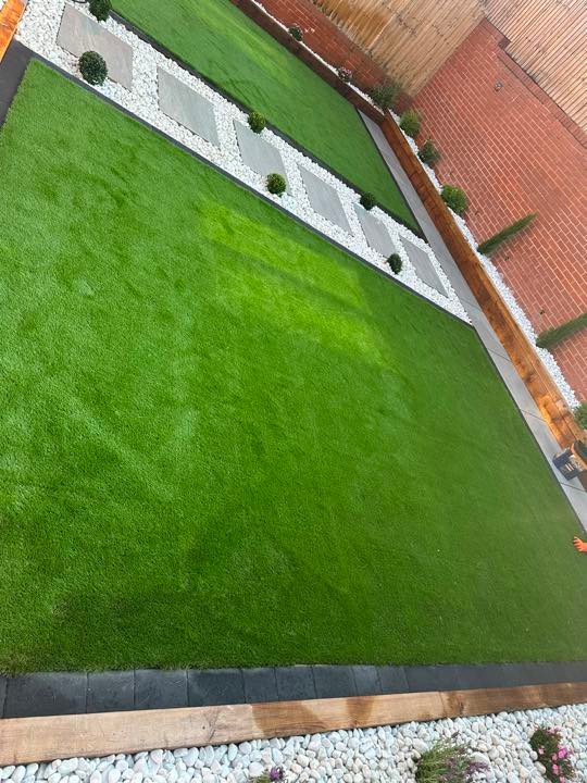 Artificial grass lawn with porcelain stepping stones and white cobbles by North West Landscapes