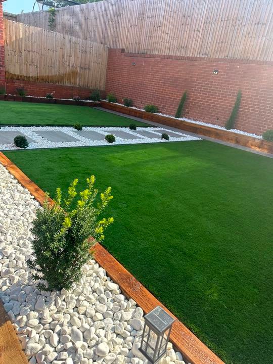 Artificial grass garden with white cobble beds and sleeper edging by North West Landscapes